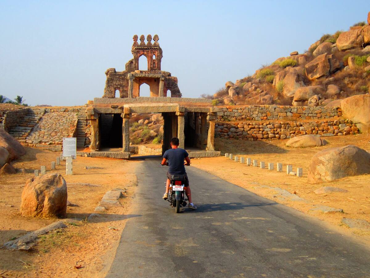 Scooter traversant une porte fortifiée de Hampi au coucher du soleil